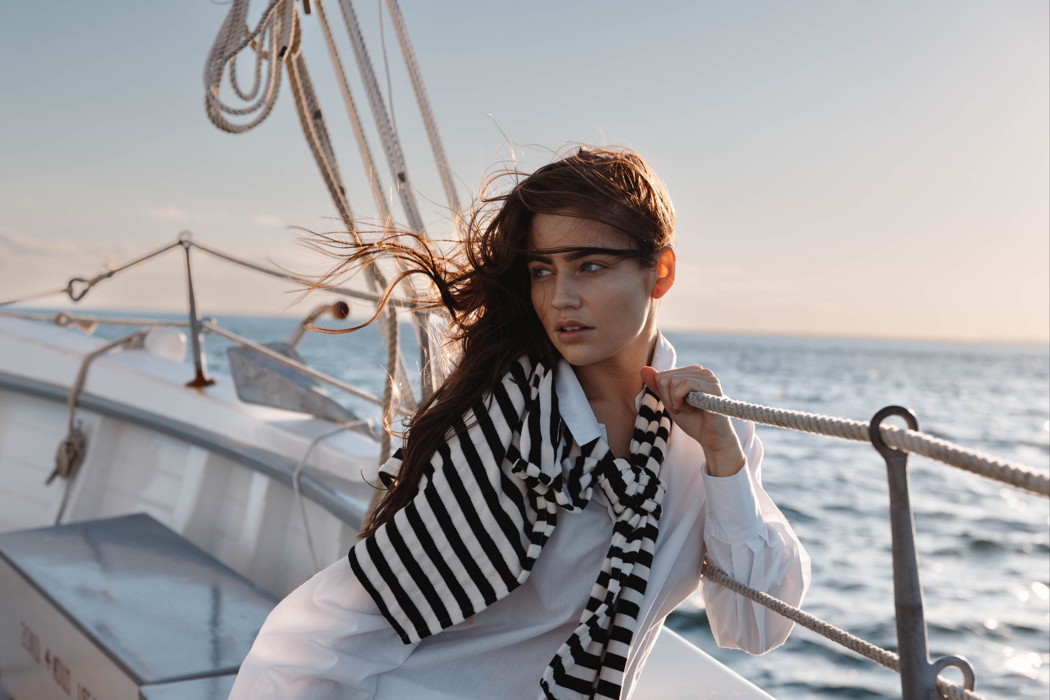 woman on sailboat with white shirt and striped sweater scarf